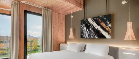 Un dormitorio moderno con una cama grande, techo de madera y vistas a un paisaje a través de un ventanal.