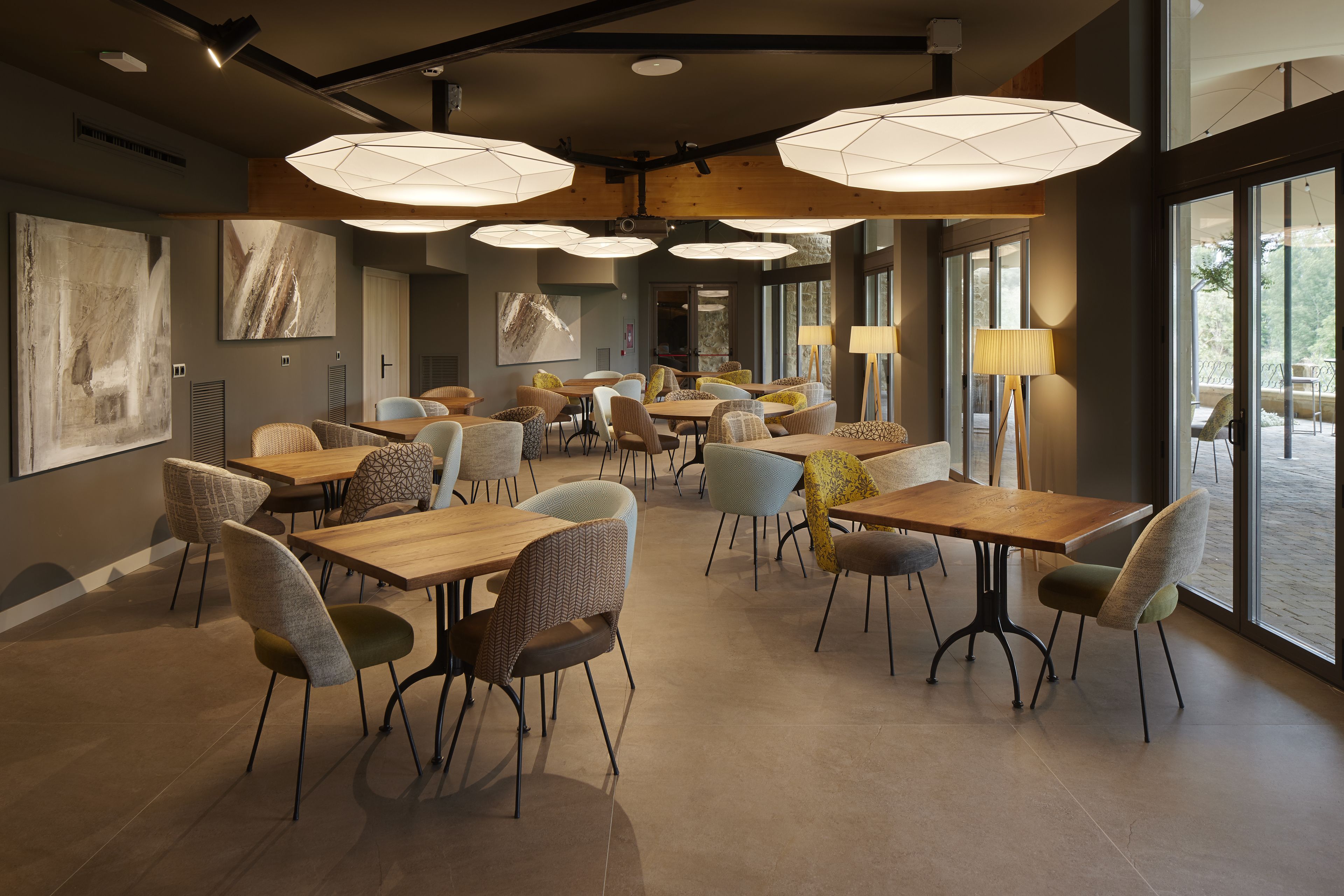 Un comedor espacioso con varias mesas y sillas, ventanas amplias e iluminación colgante moderna.