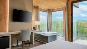 Una habitación de hotel moderna con una cama grande, un escritorio con silla, televisión y vistas al exterior a través de amplias ventanas.