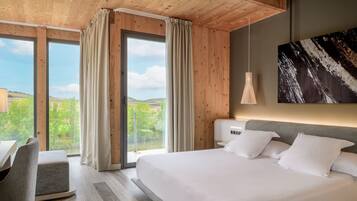 A modern bedroom with a large bed, a desk, and a view of the outdoors.