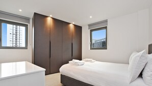 Ein modernes Schlafzimmer mit einem großen Bett, einem Kleiderschrank und zwei Fenstern.