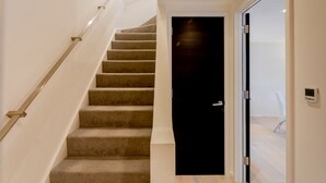 Eine Treppe mit Teppichstufen und einem Metallgeländer, das zu einer schwarzen Tür mit Griff führt.