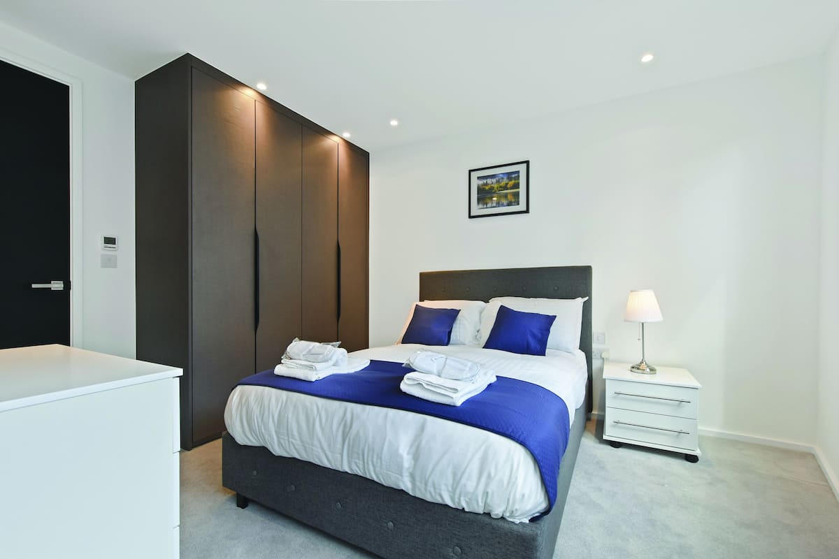A modern hotel room with a large bed, a nightstand, a wardrobe, and a picture on the wall.