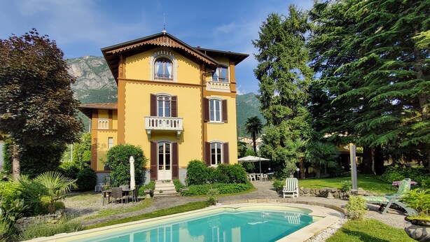 A yellow building with a pool, surrounded by greenery and mountains. - Villa Laura (Lierna)