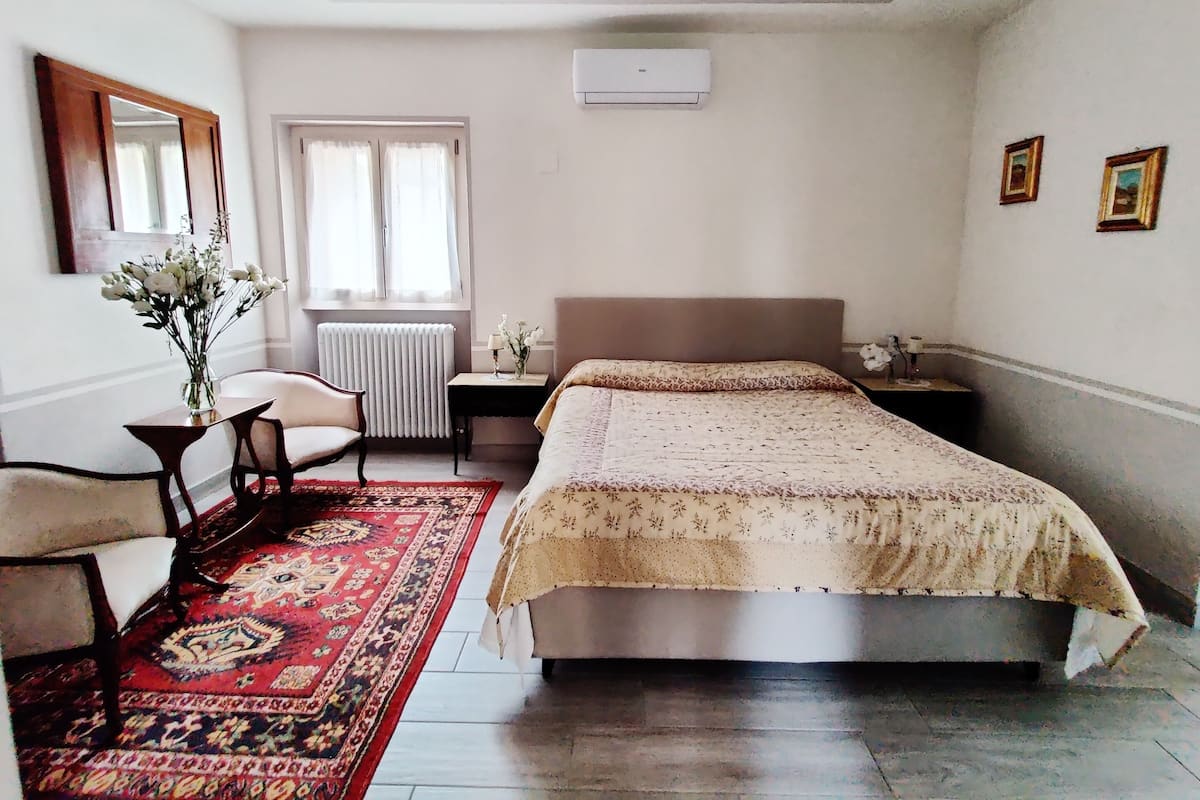 A bedroom with a bed, a chair, a table, a radiator, and a window.