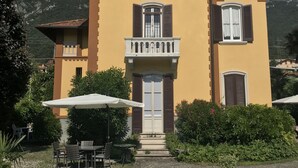 A two-story building with a balcony, a pool, and a mountainous backdrop. - Villa Laura (Lierna)