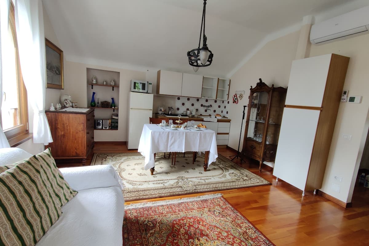 A cozy living room with a sofa, a dining table set for four, and a kitchen area with cabinets and a microwave.