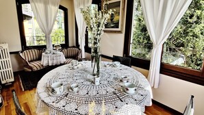 A cozy room with a round table set for tea, featuring a lace tablecloth, white cups, and saucers. There is a chair with a striped cushion, a vase with white flowers, and a painting on the wall. - Villa Laura (Lierna)