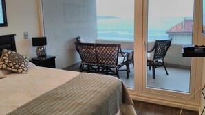 Habitación de hotel con cama, mesita de noche, una mesa con sillas y un balcón con vistas al mar.