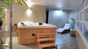 Un baño moderno con una bañera de madera, una zona de ducha y un rincón de descanso con una silla y plantas.