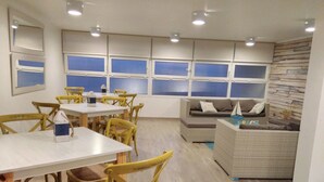 Un comedor con sillas y mesas de madera, un sofá y un ventanal con persianas.