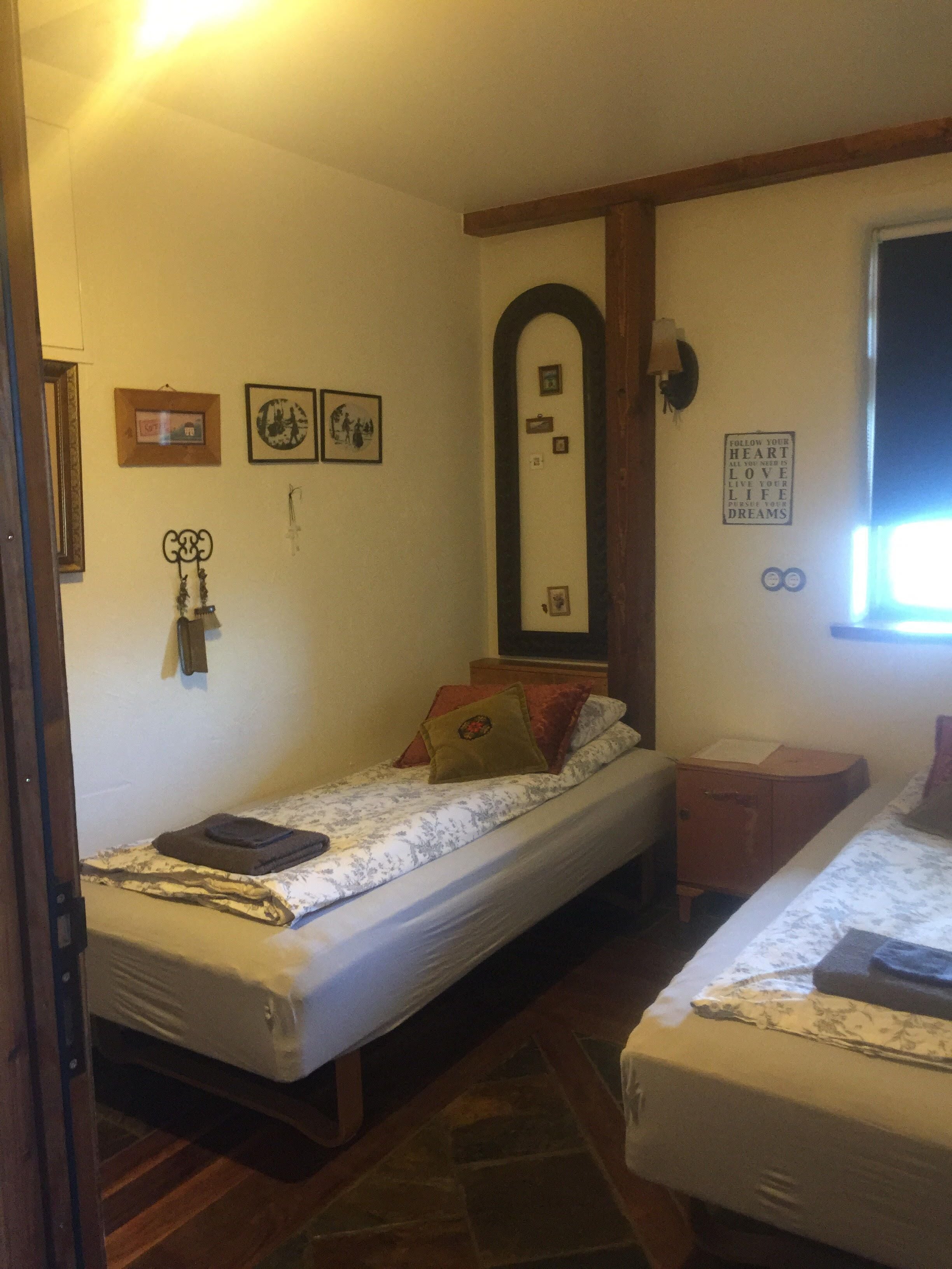 Un dormitorio pequeño y acogedor con dos camas individuales, un armario de madera, un espejo y algunas decoraciones en la pared.
