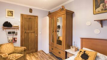 Una habitación con un armario de madera, un sofá, una cama con un cojín estampado y un estante en la pared con adornos.