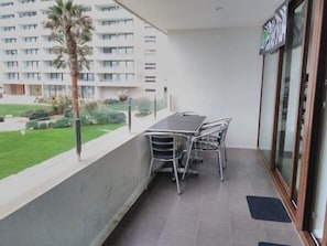 A balcony with a table and chairs, overlooking a grassy area and a building with multiple windows.