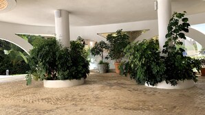 Un vaste espace intérieur doté de nombreuses colonnes, de plantes en pot et d’un sol carrelé.