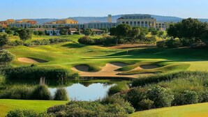 Un parcours de golf avec des bunkers, un étang et des bâtiments en arrière-plan.