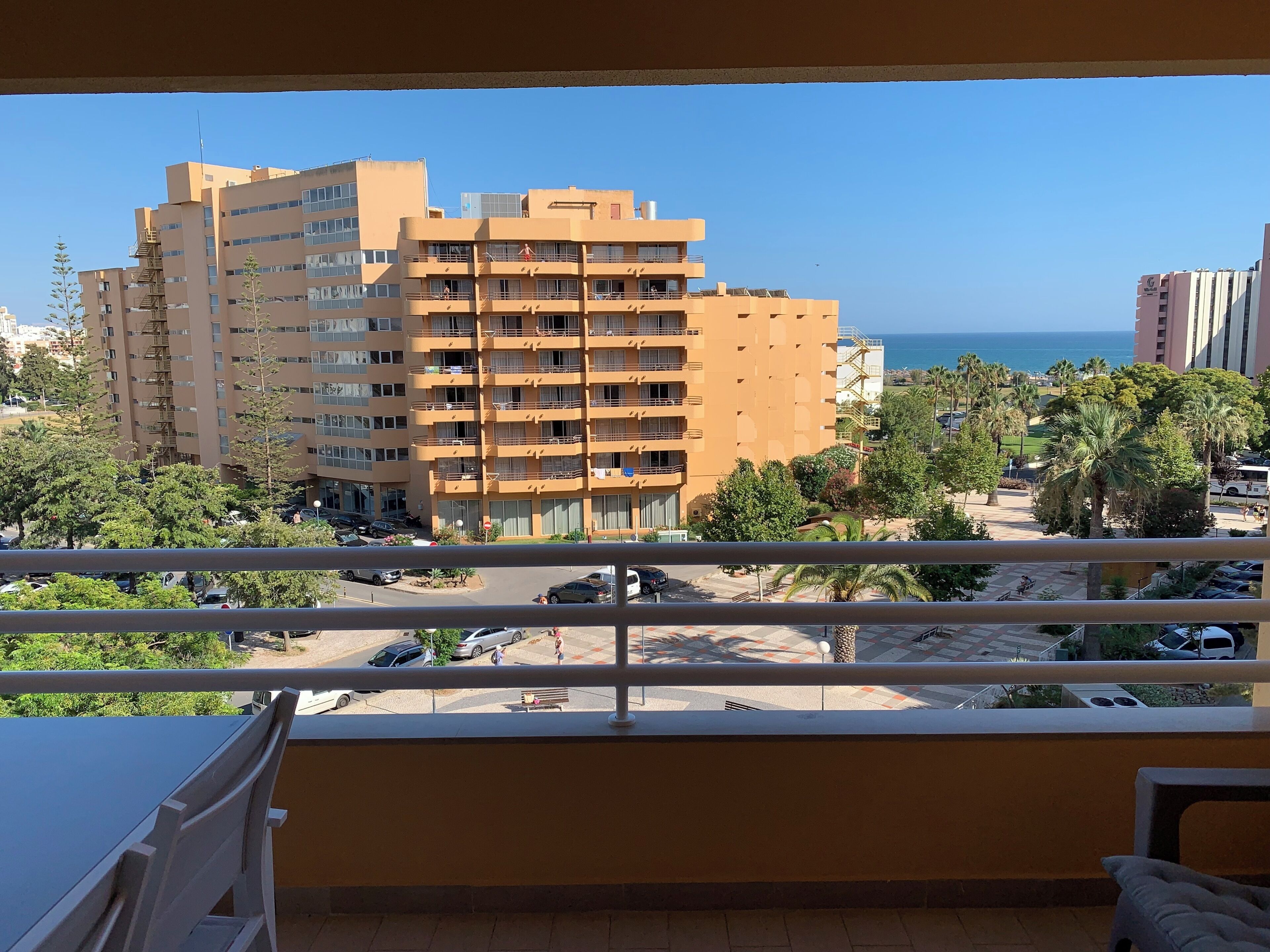 Een balkon met uitzicht op een meerhoog gebouw, een parkeerplaats en een strand met palmbomen.