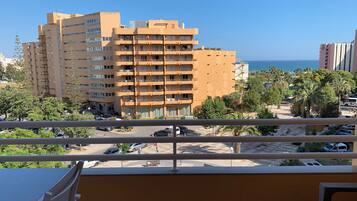 Een balkon met uitzicht op een meerhoog gebouw, een parkeerplaats en een strand met palmbomen.