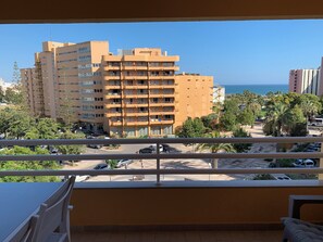 A balcony with a view of a multi-story building, a parking area, and a beach with palm trees. - Discovery Apartment Vilamoura (Loulé)