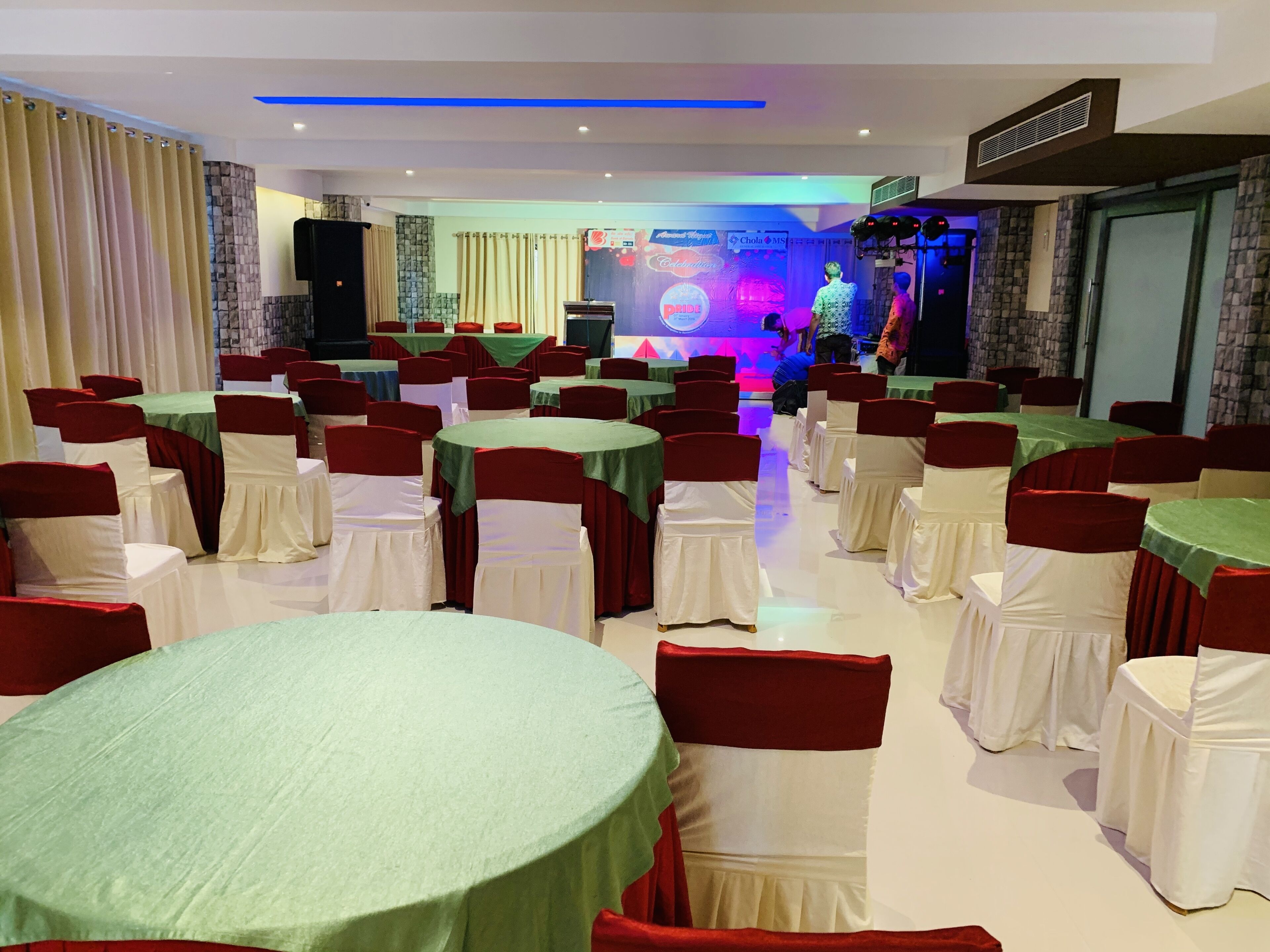 A banquet hall with round tables and chairs, a stage with performers, and a DJ booth.