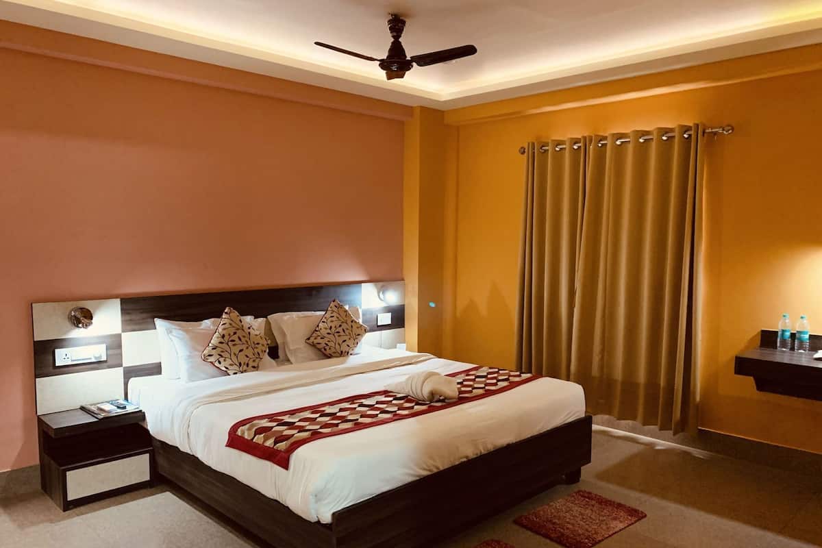 A hotel room with a bed, nightstands, a ceiling fan, a window with curtains, and a small shelf with water bottles.