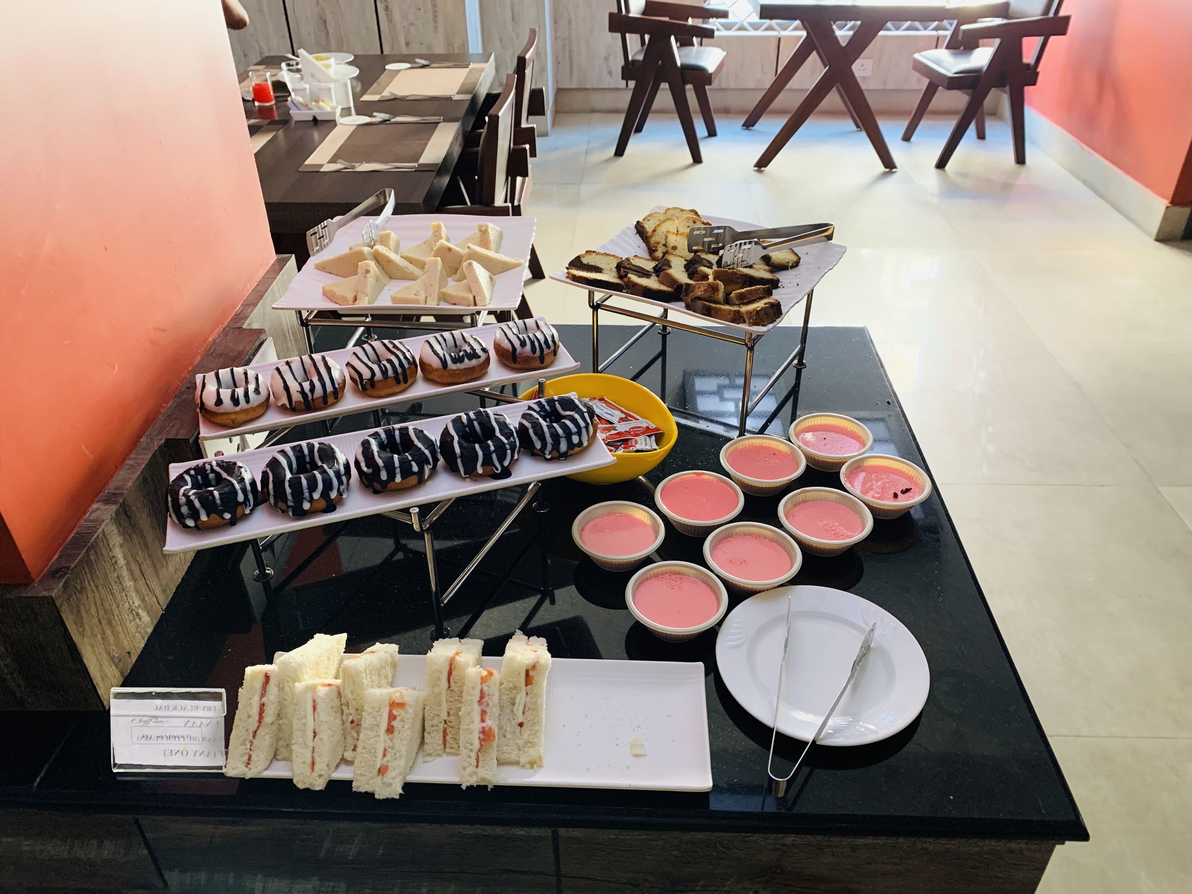 A buffet table with various food items including donuts, sandwiches, and desserts.