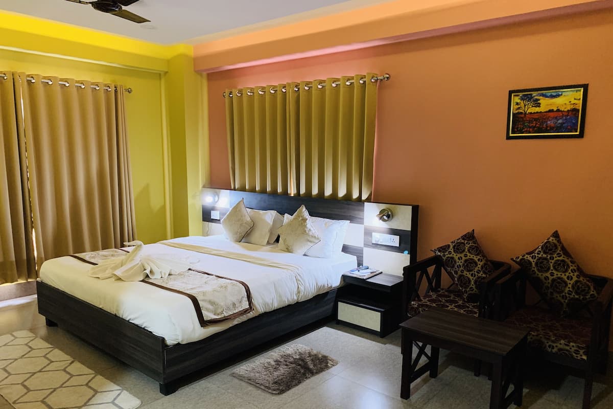 A hotel room with a bed, bedside table, chair, curtains, and a painting on the wall.