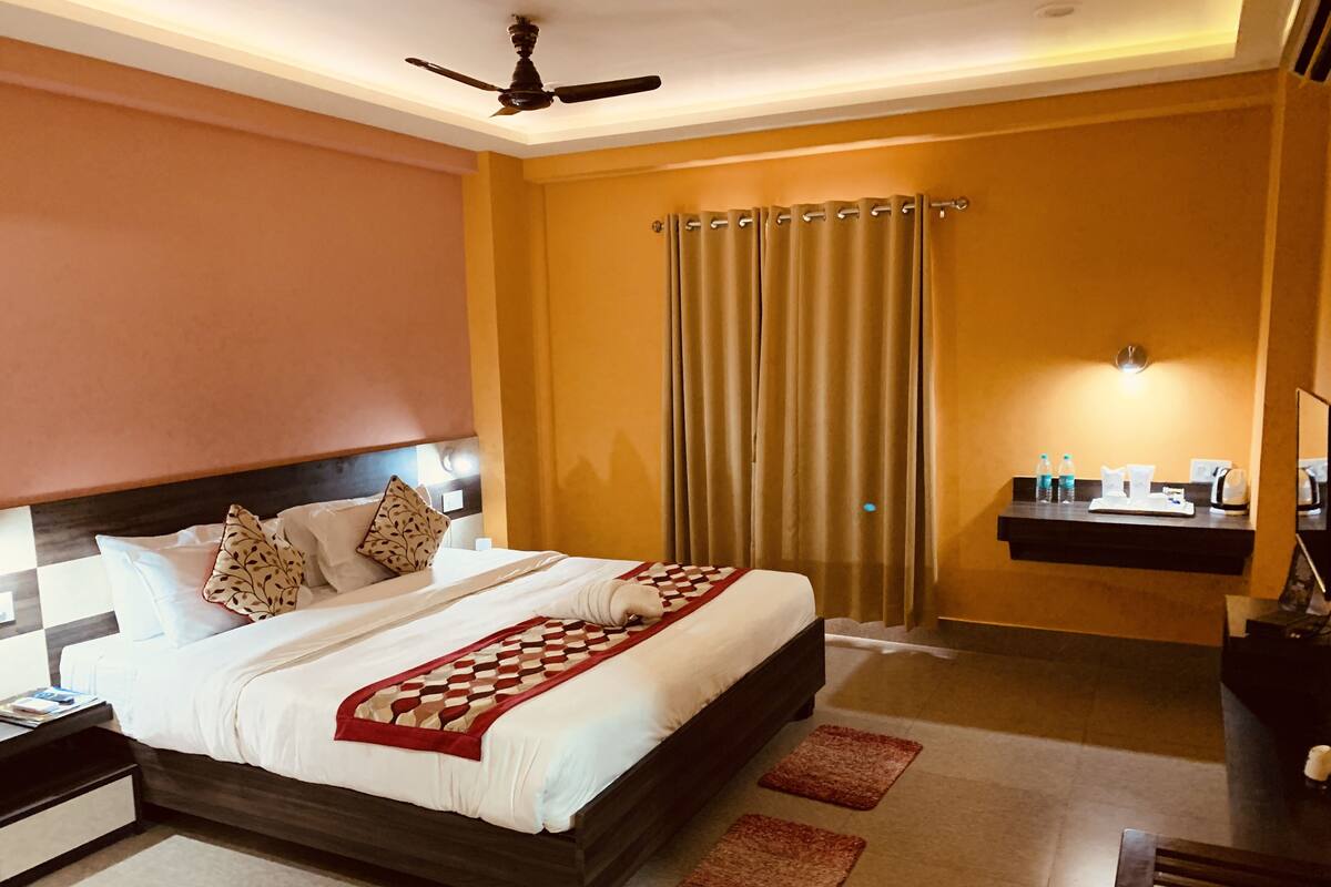 A hotel room with a bed, a nightstand, a desk, a chair, a ceiling fan, and a window with curtains.