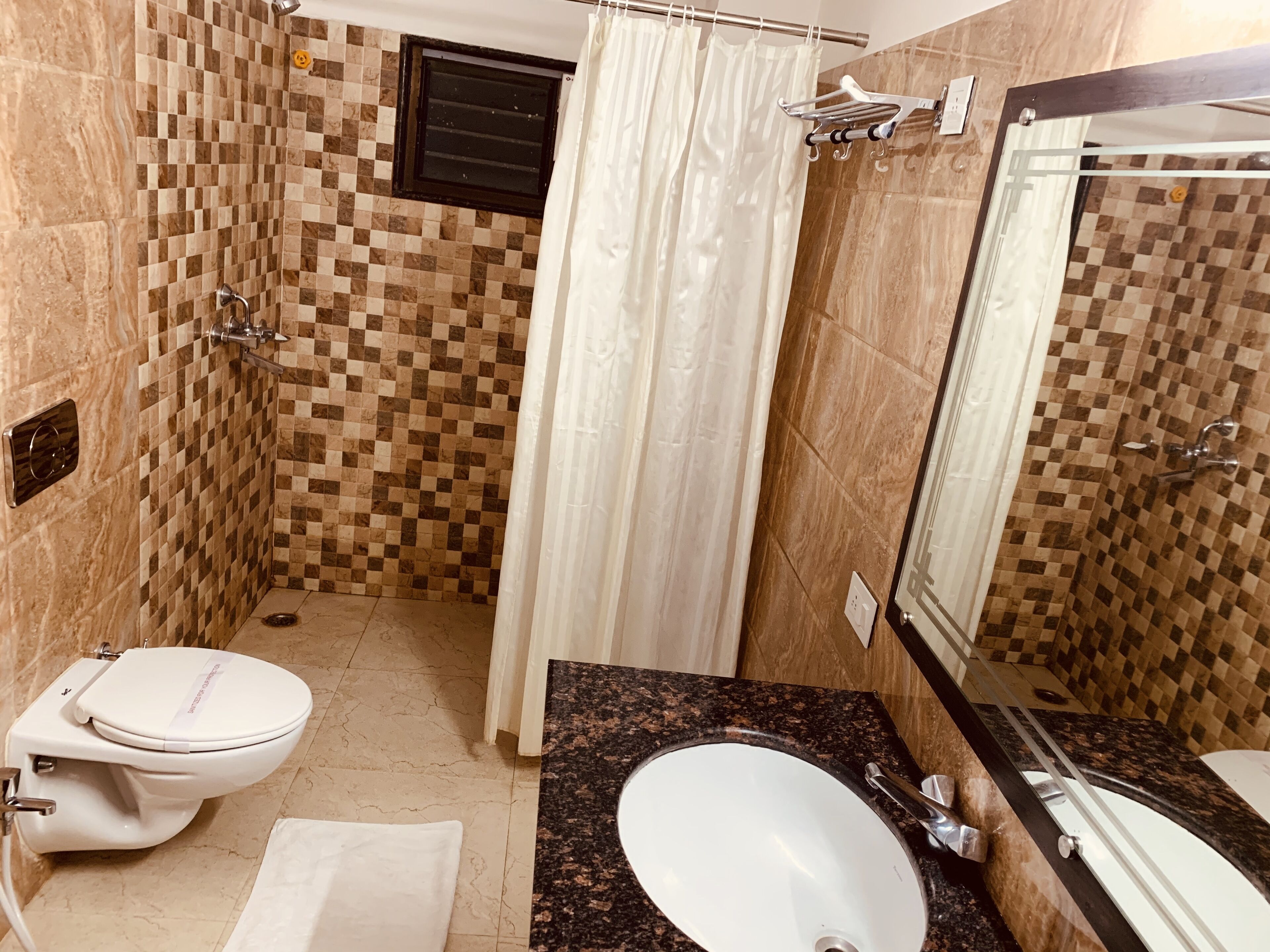 Un bagno con parete rivestita di piastrelle a scacchi, un water, un lavandino e una doccia con tenda.