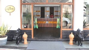 Entrada de hotel com receção, relógio e placa com o nome do hotel.