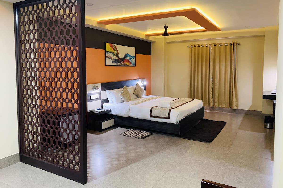 A modern hotel room with a large bed, a decorative screen, a painting on the wall, and a ceiling light fixture.