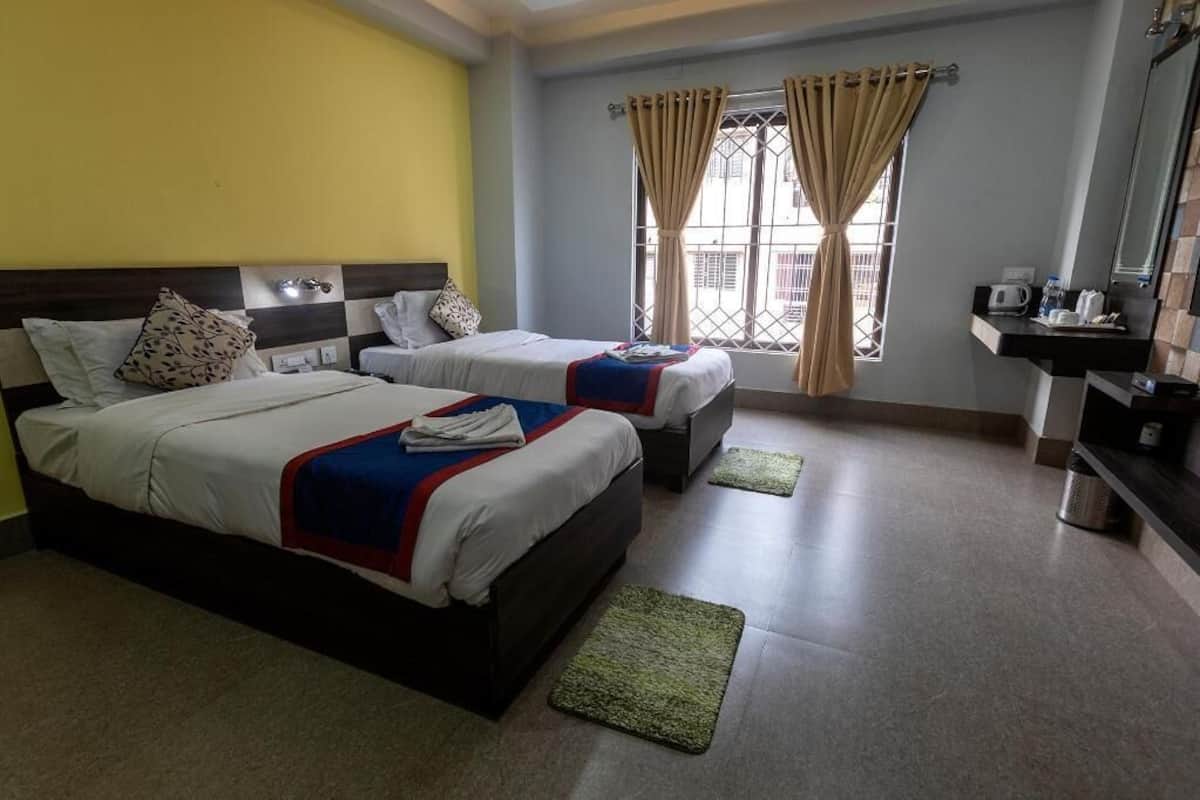 A hotel room with two beds, a small bathroom, and a window with curtains.