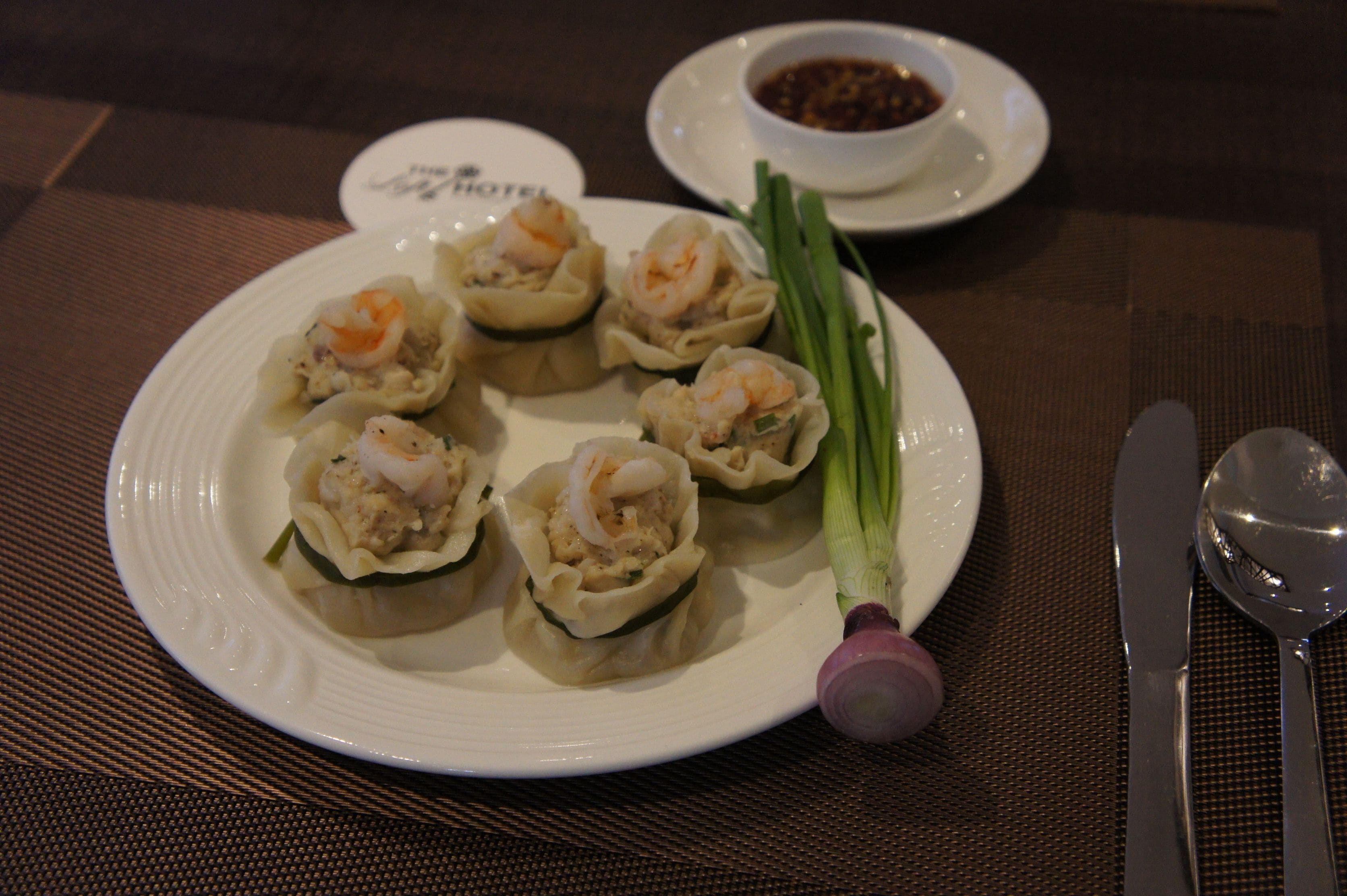 Un plato de dumplings con salsa para mojar y cebollines sobre una mesa.