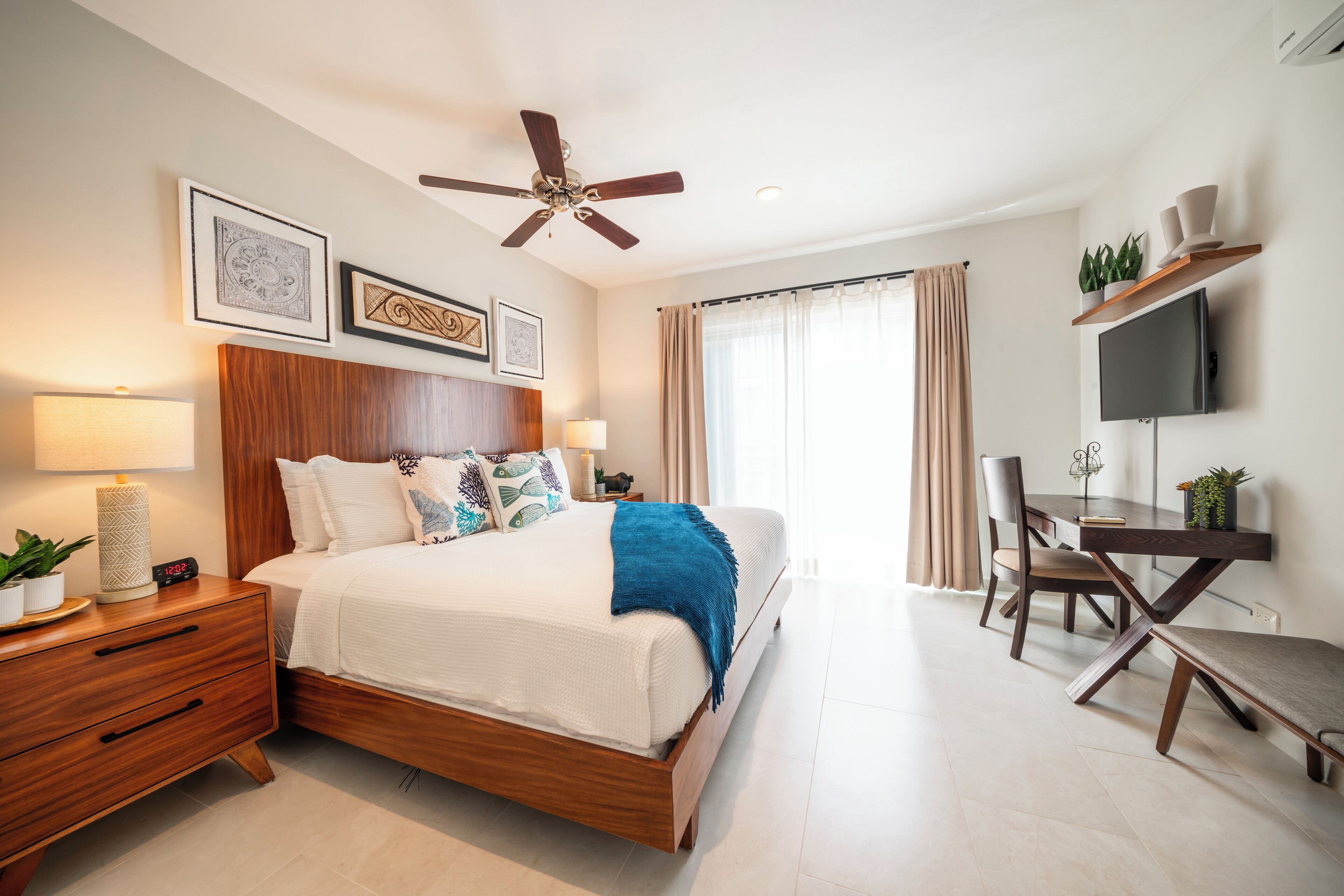 A modern bedroom with a wooden bed, bedside tables, a desk, and a ceiling fan.