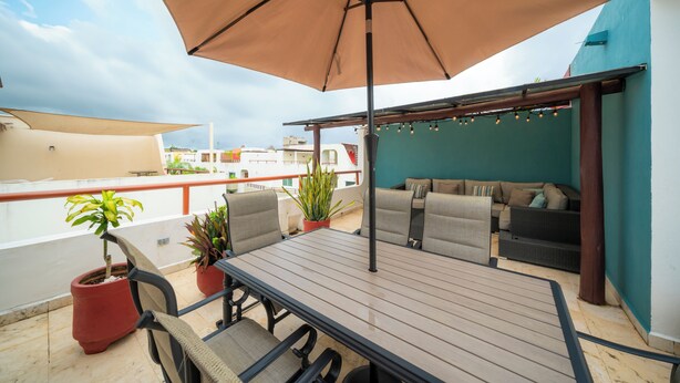 A rooftop terrace with a wooden table, chairs, a sofa, and potted plants. - Sol Tranquilo by NAS (Playa del Carmen)