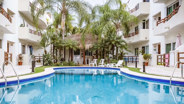 Piscina rodeada por palmeiras e edifícios brancos com varandas.