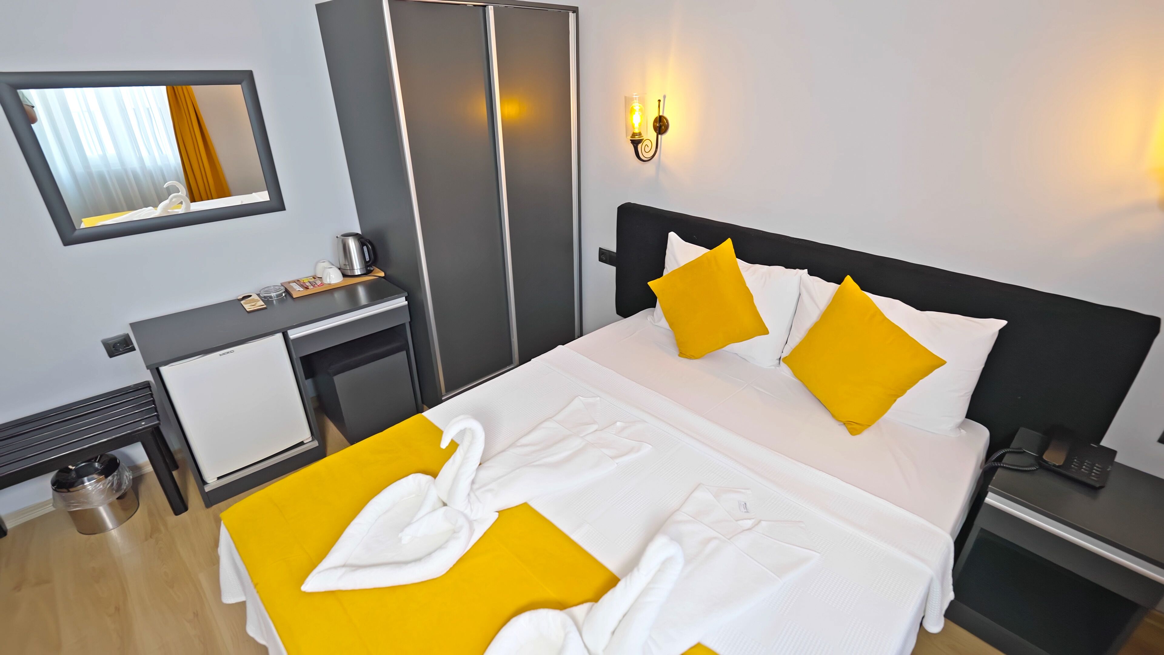 A hotel room with a bed, a desk, a wardrobe, and a mirror.