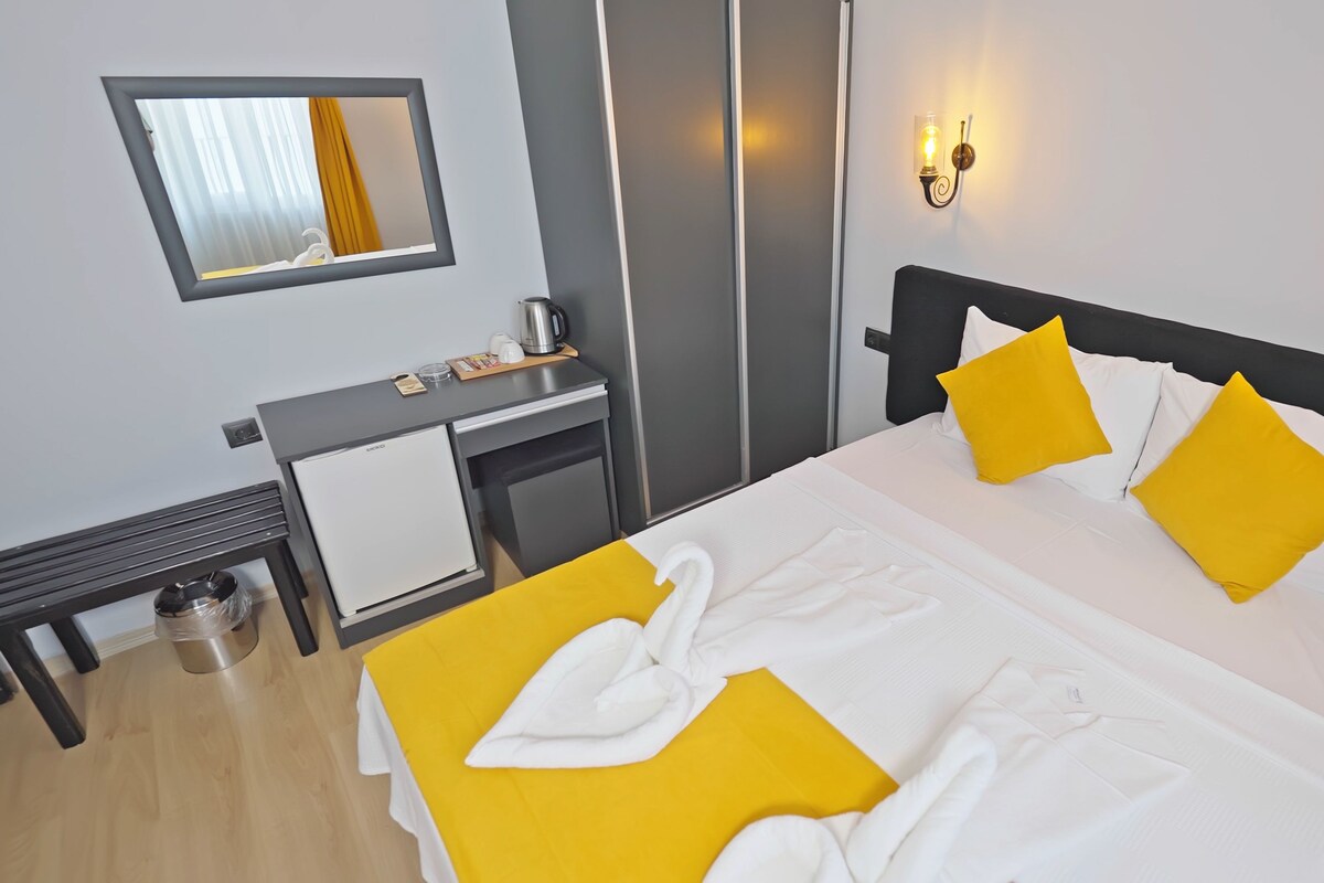 A hotel room with a bed, a desk, a mirror, and a wall-mounted light fixture.