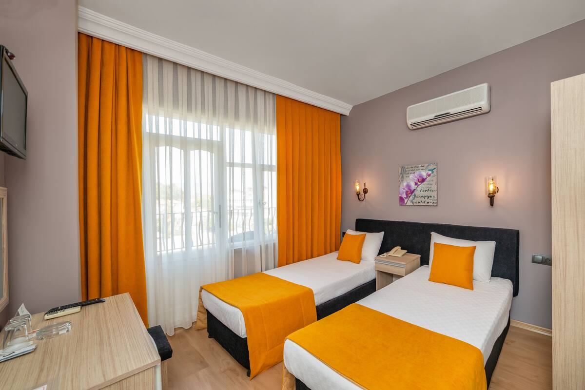 A hotel room with two beds, a desk, and a window with curtains.
