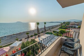 A balcony with a view of a beach, a pool area, and a cityscape in the background. - Yasemin Hotel (Fethiye)