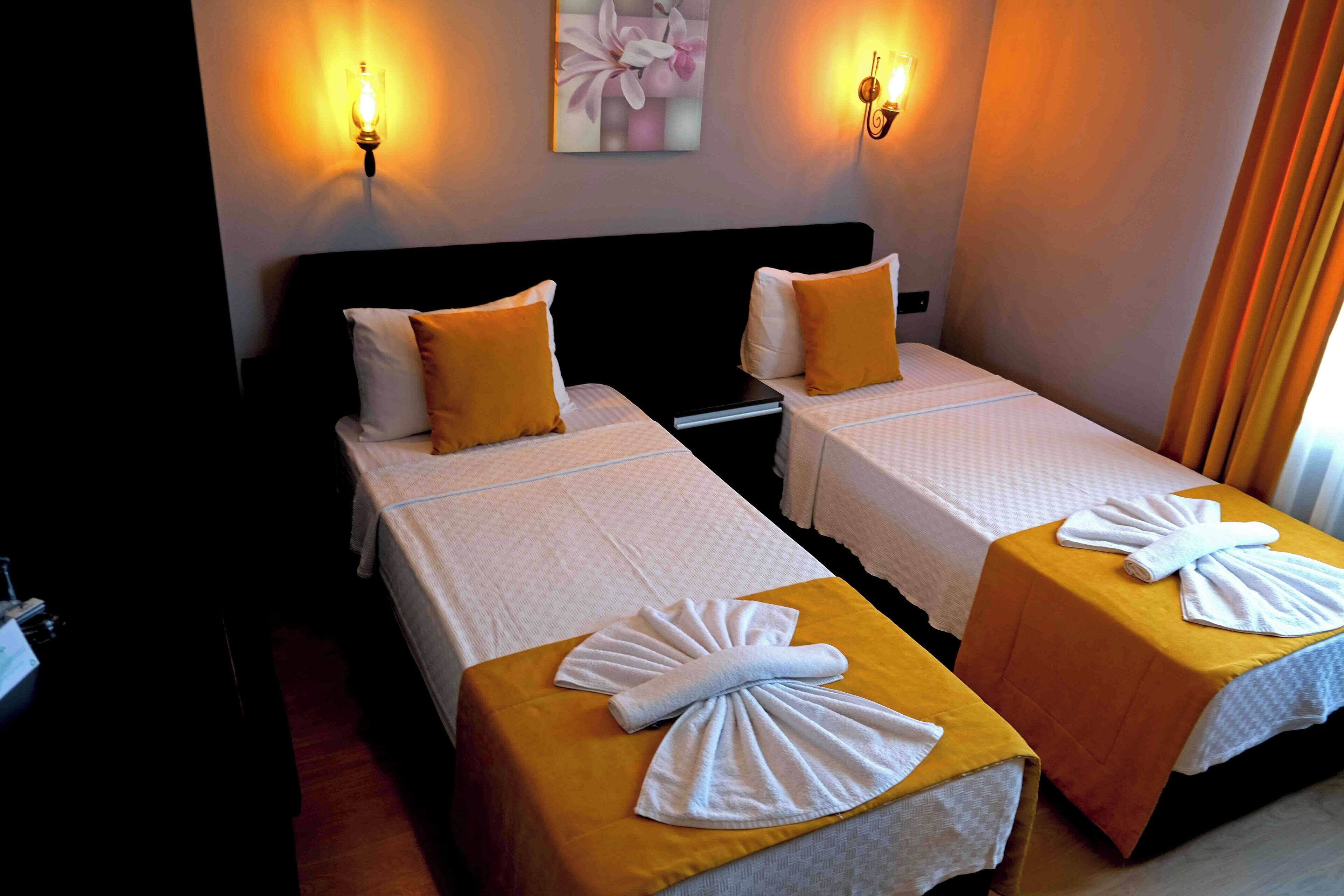 Two single beds with white linens and yellow bedspreads, each with a towel folded on top.