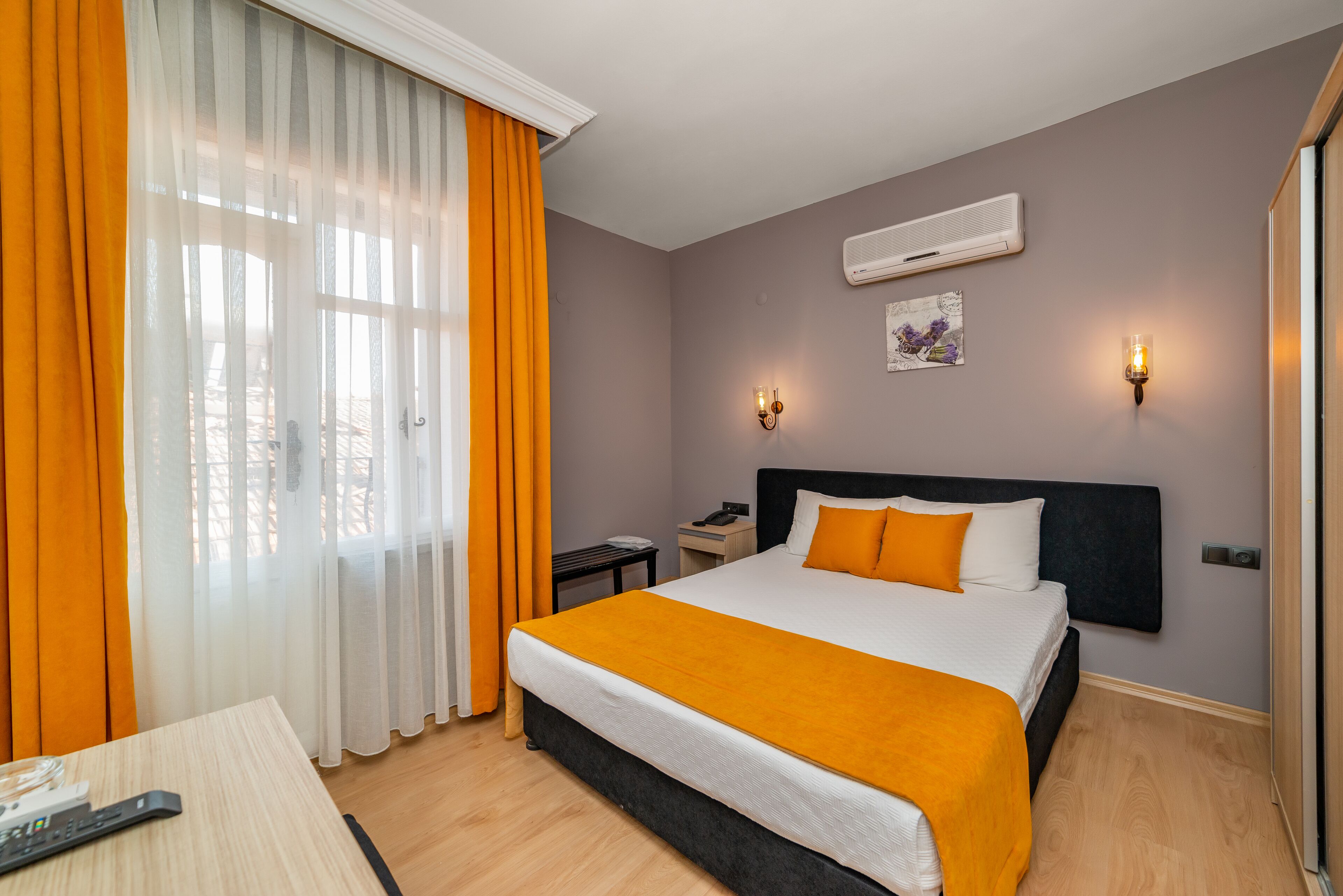 Une chambre d’hôtel avec un lit, une table de chevet, un bureau et une fenêtre avec des rideaux.