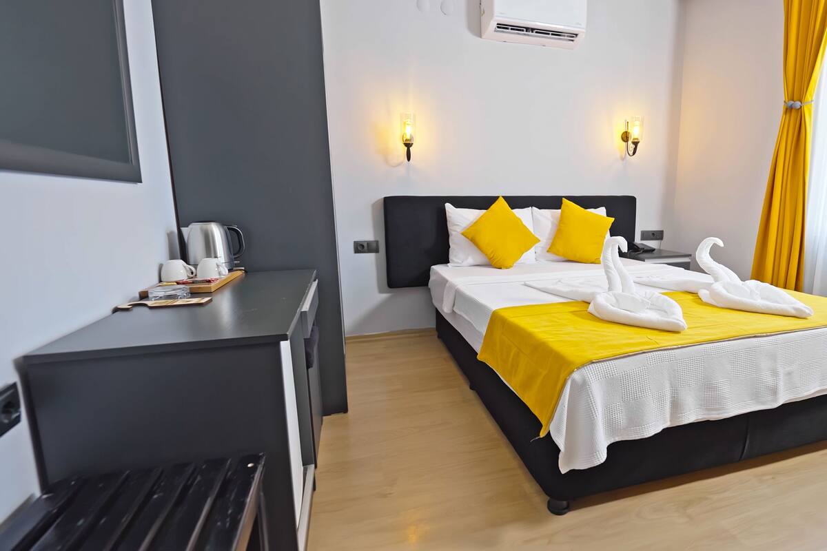 A hotel room with a bed, bedside table, and a desk with a kettle.