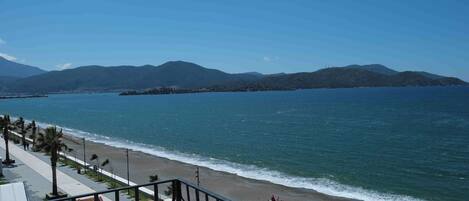 A coastal view with a beach, a promenade, and mountains in the background.