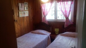 Una habitación pequeña y acogedora con paredes de madera y dos camas individuales con ropa de cama estampada.