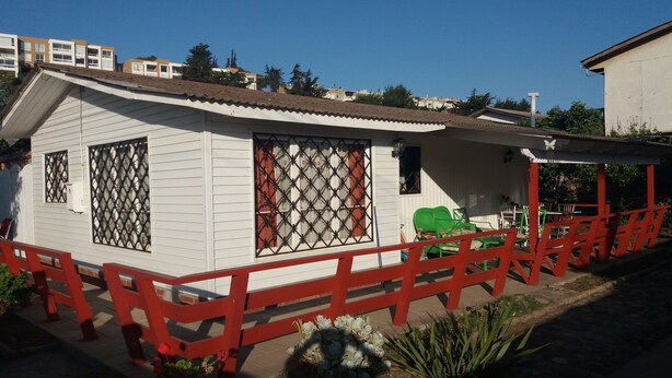 Un petit bâtiment blanc, avec une clôture rouge, de grandes fenêtres dotées de grilles métalliques et un porche couvert avec des chaises vertes.