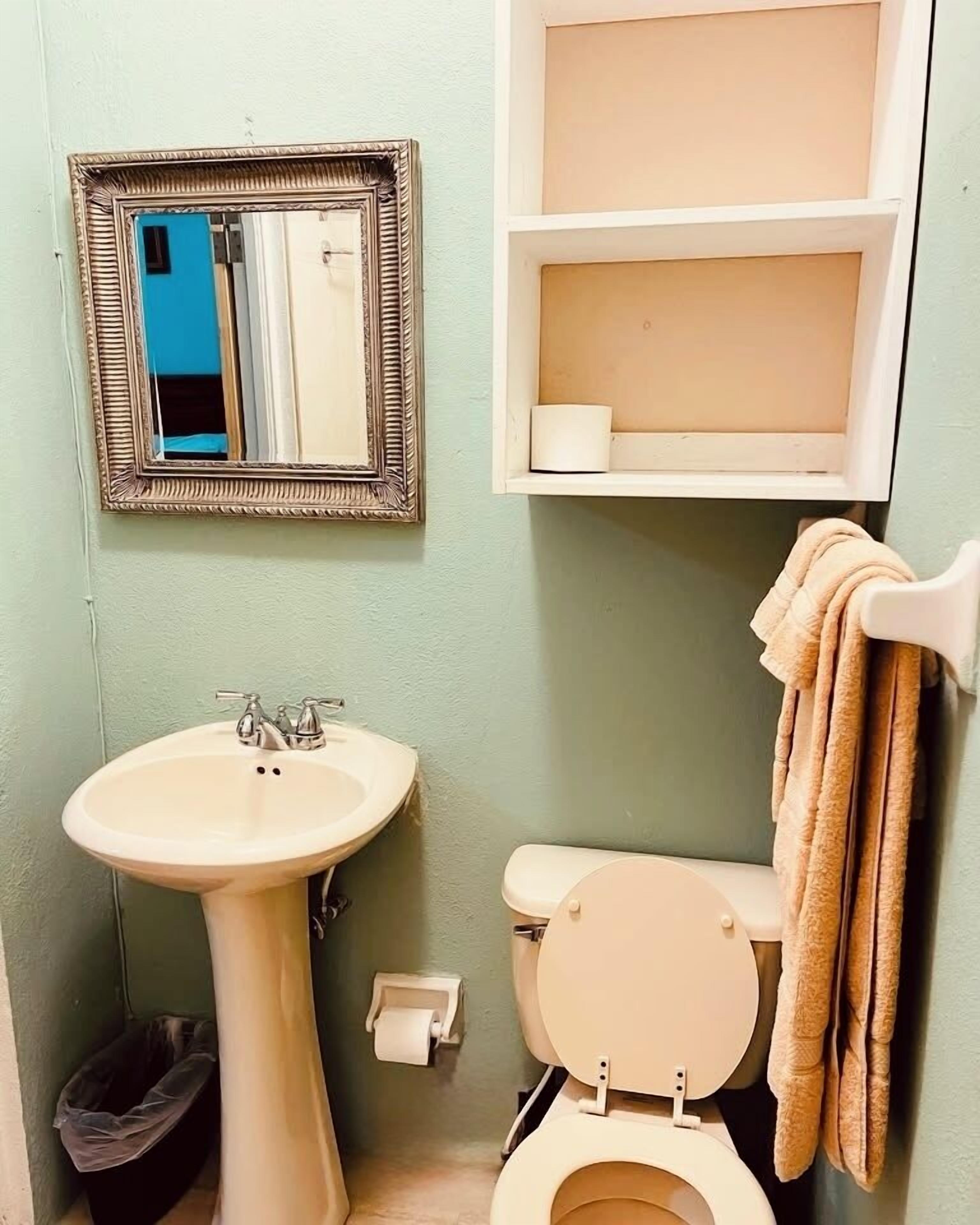 A bathroom with a pedestal sink, toilet, and a mirror with a picture frame.