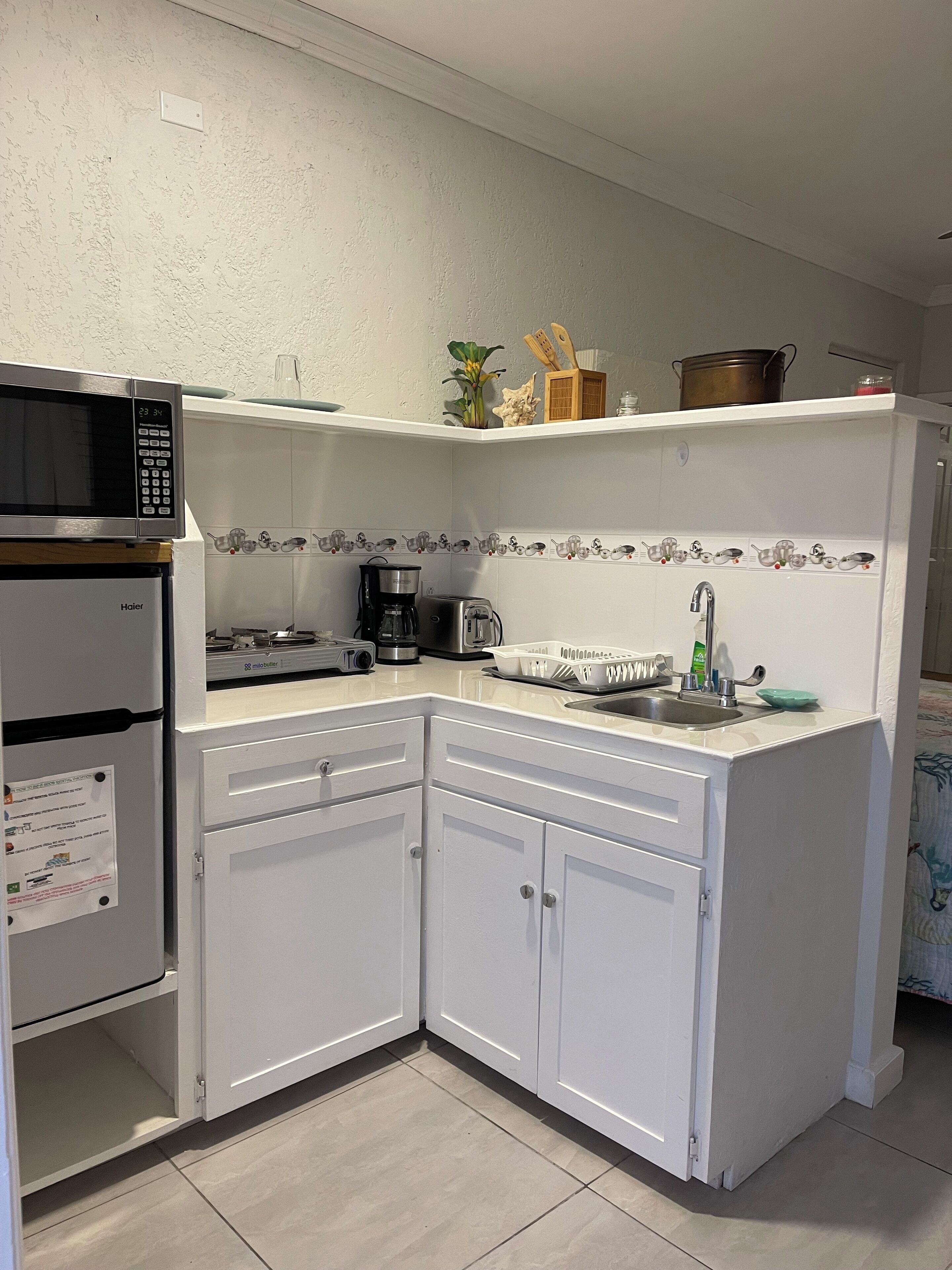 A compact kitchen with white cabinets, a microwave, a coffee maker, and a sink.