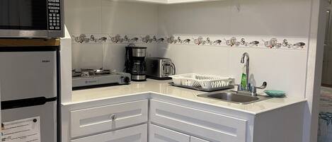 A compact kitchen with white cabinets, a microwave, a coffee maker, and a sink.