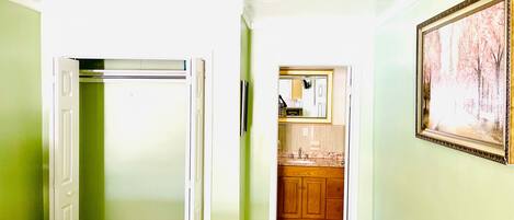 A hallway with a door leading to a bathroom, a small kitchen area, and a framed picture on the wall.